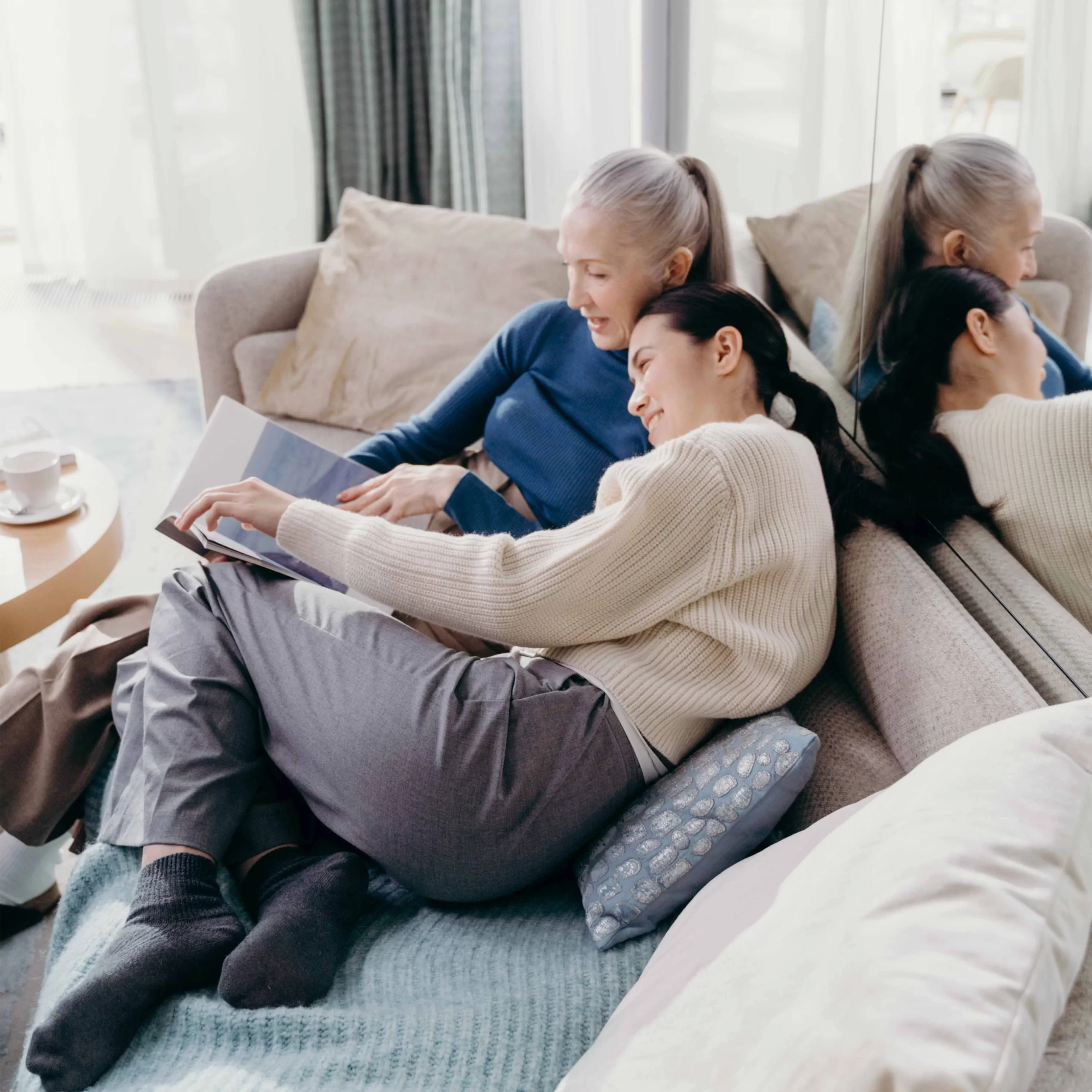 Mother and daughter sitting on a sofa together, smiling as they look through a photo album