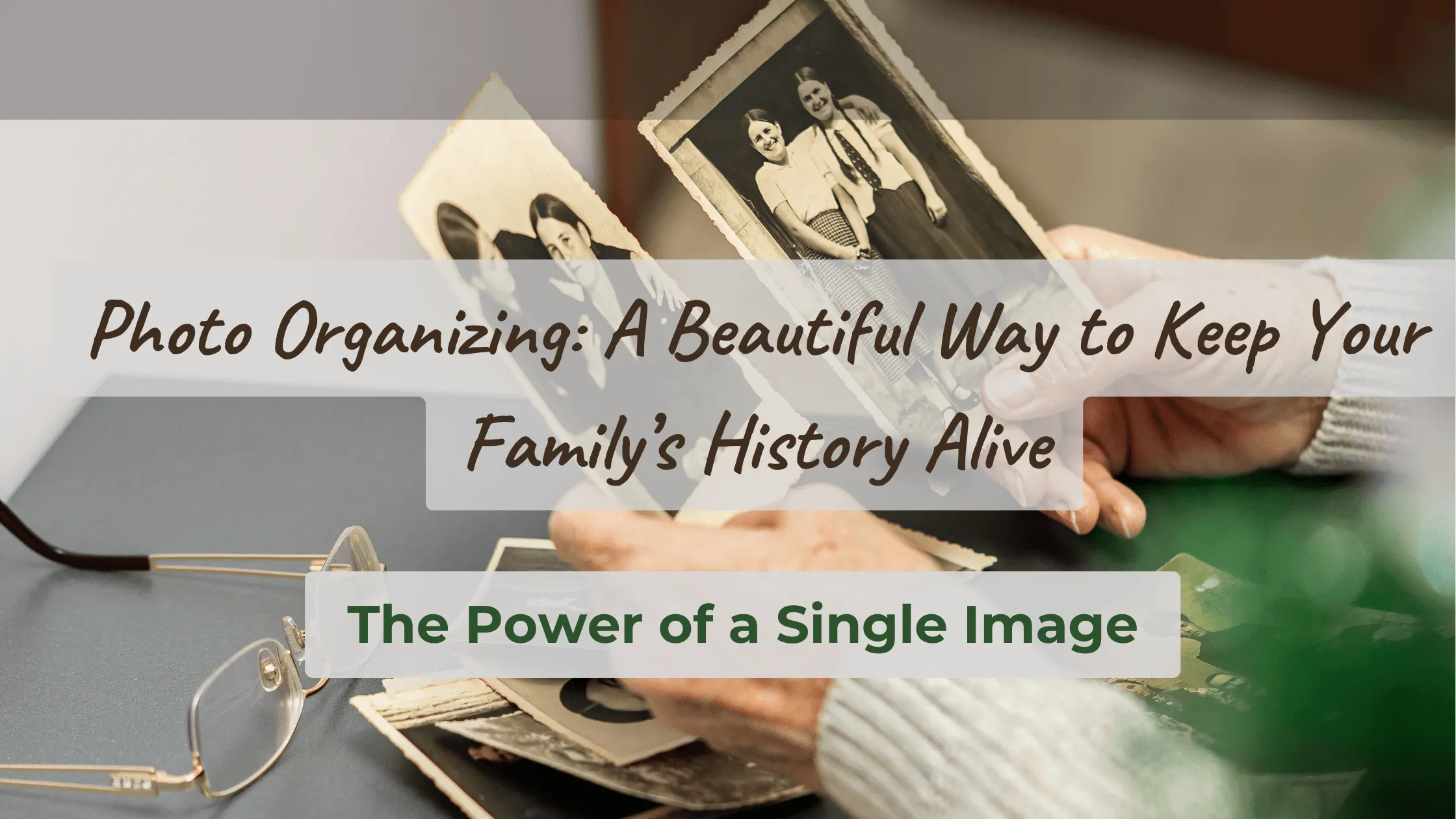 Hands of an older adult holding two vintage photos with more photos on a table beside reading glasses