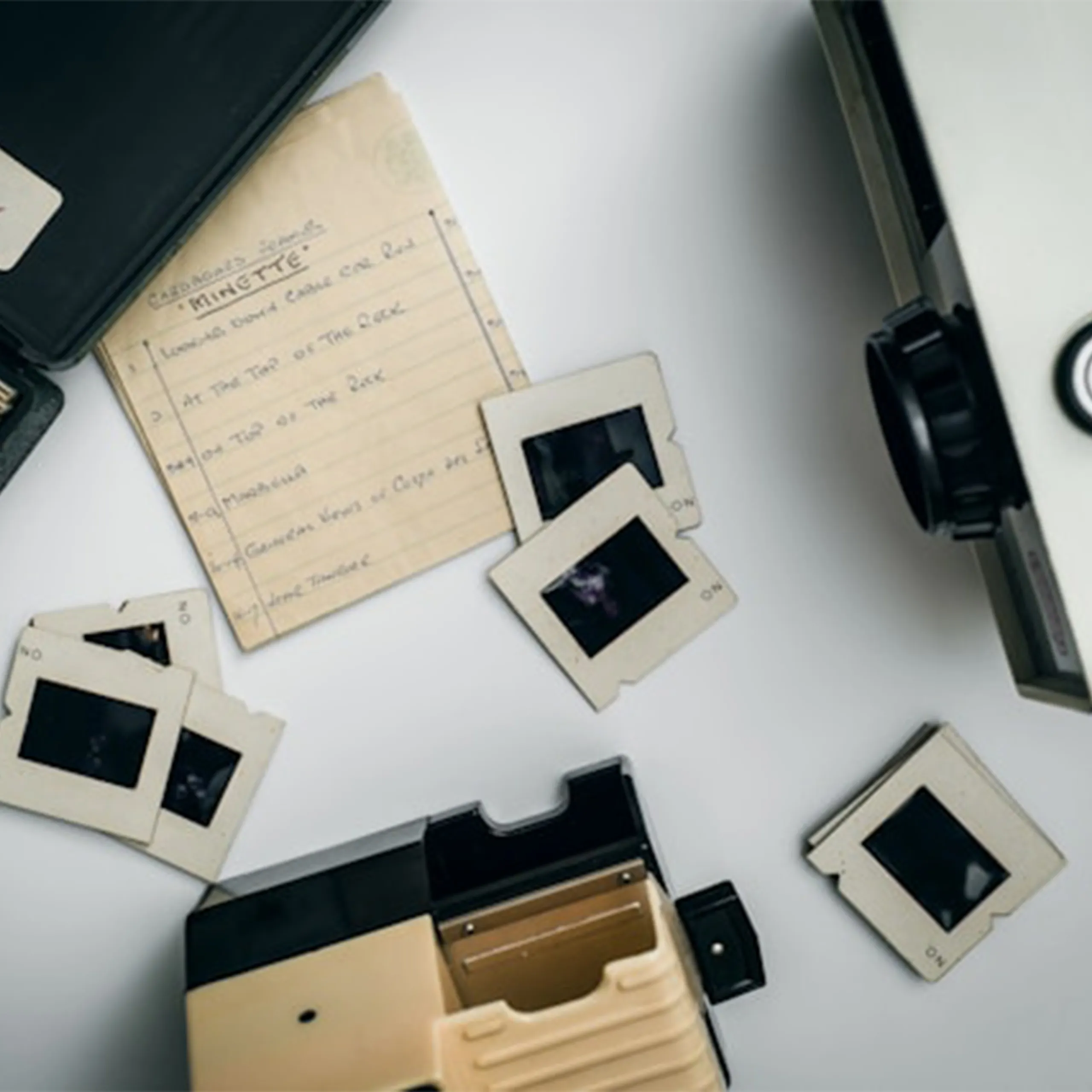Slide Projector and Loose Slides – Your Photo Assistant Slide projector on a table surrounded by loose photo slides and a paper content list